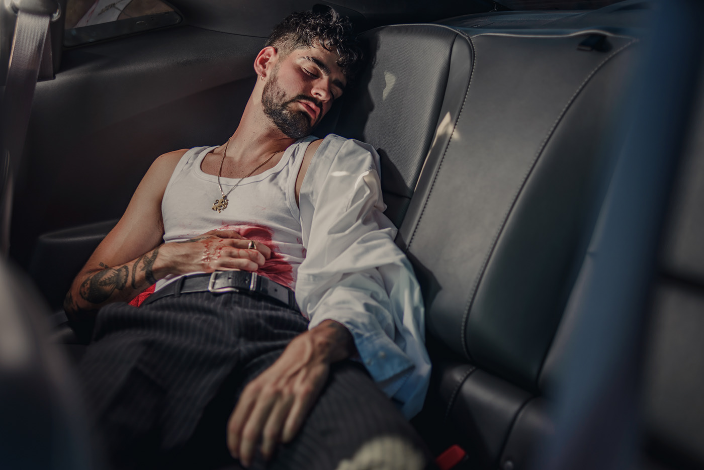 Tiroteo — A man wearing a white shirt and black pants is laying down in a car.