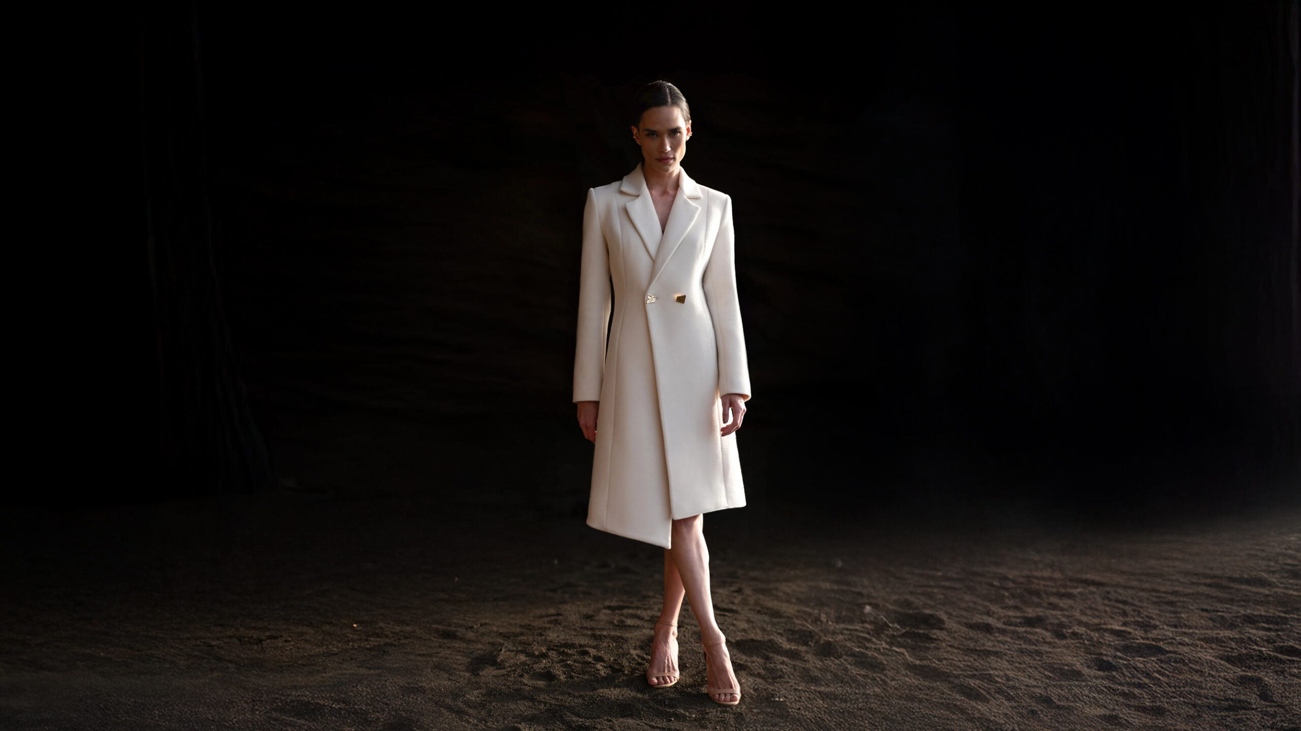 Ember by Inti — A woman wearing a white coat stands on a beach.