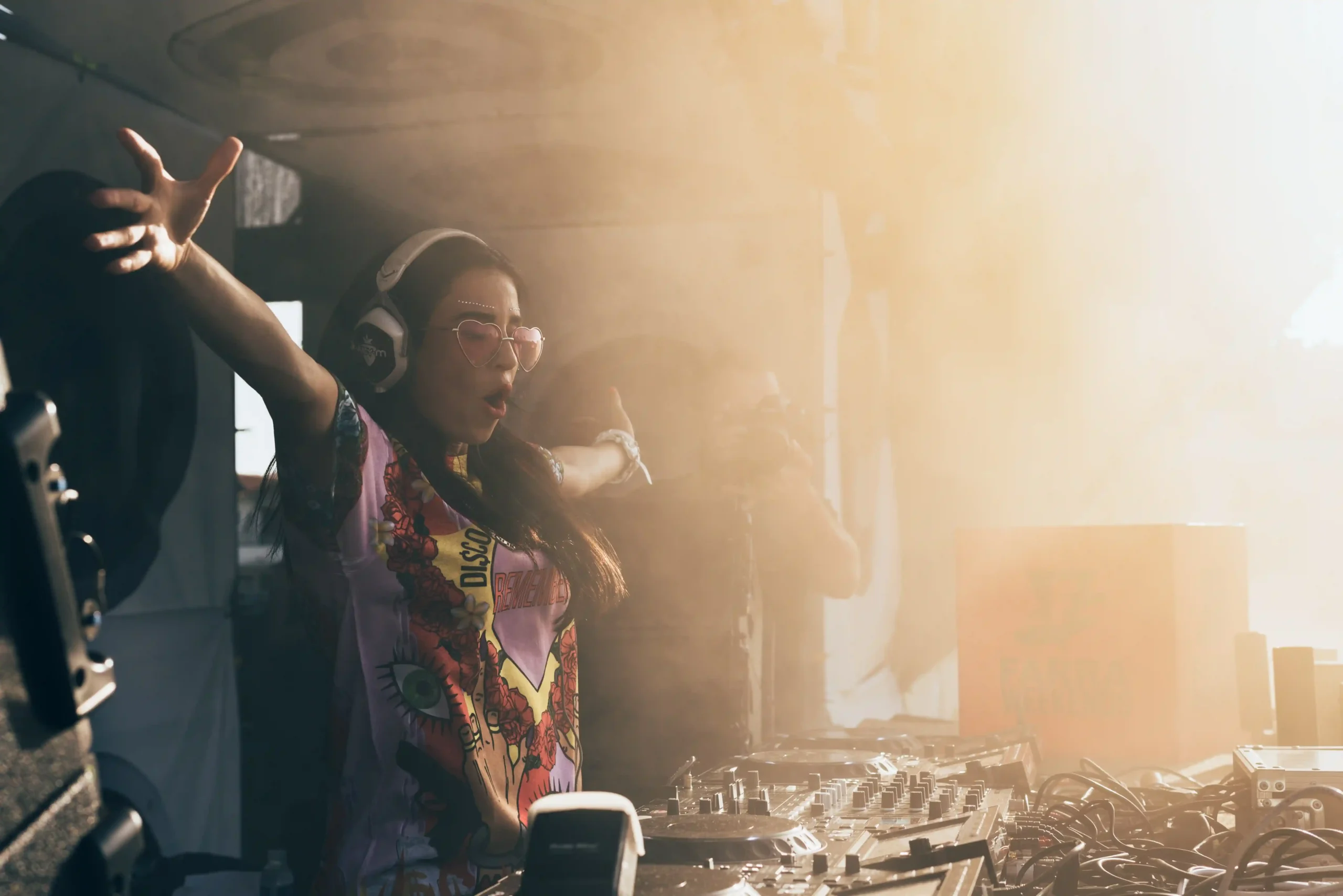 Farra World — A woman wearing headphones and a pink shirt is dancing in front of a DJ booth.