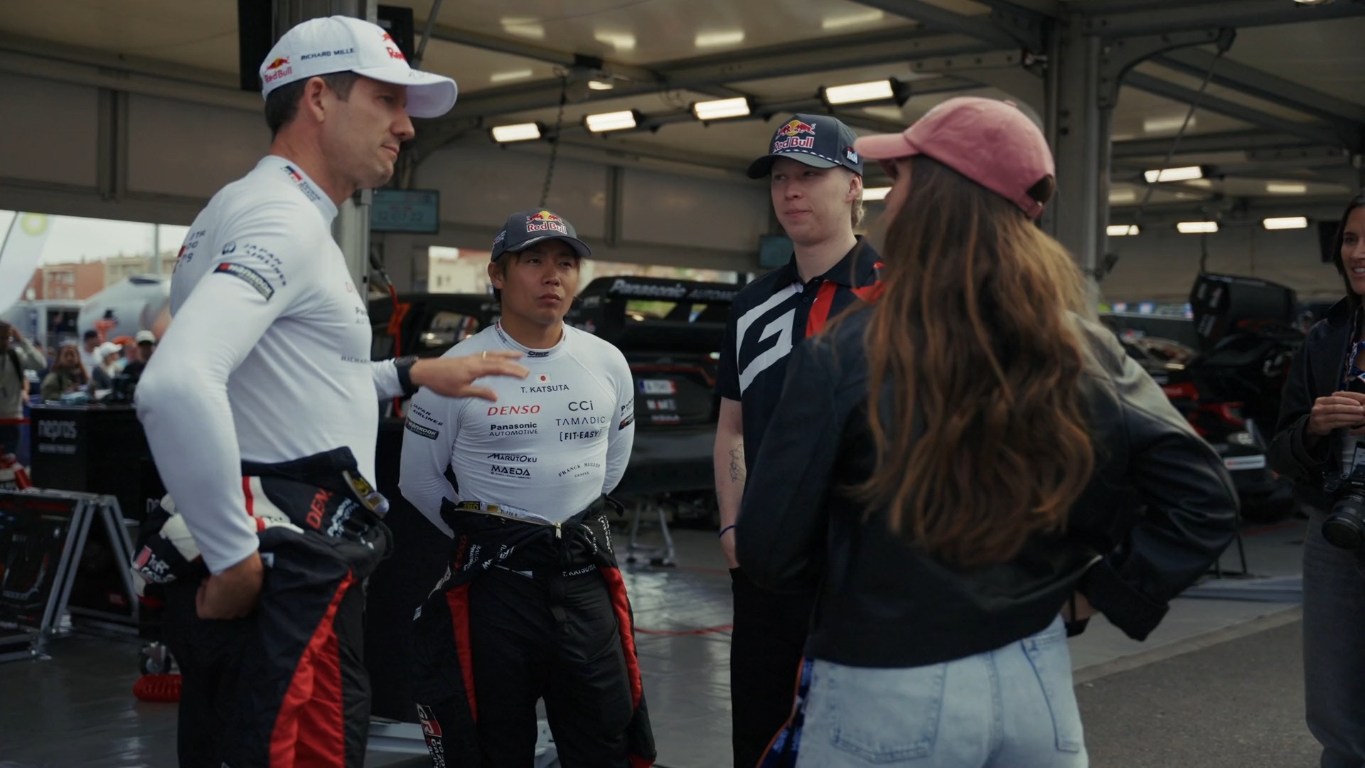 RedBull WRC — A group of people wearing racing uniforms are standing in a garage.